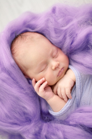 sleeping newborn girl in the purple violet pink wool background, close-upの写真素材