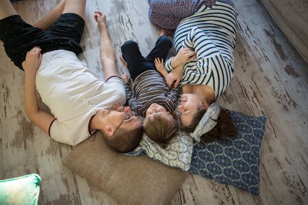 Happy pregnant mother, father and son Toddler lying on the floor, hugging,. Real interior, toning, lifestyle,casual styleの写真素材