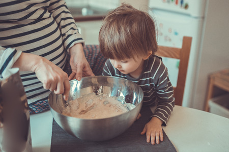 young pregnant mother with dreadlocks is preparing in the kitchen with her son Toddler, make the...