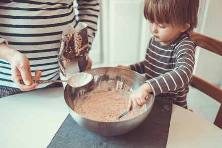 young pregnant mother with dreadlocks is preparing in the kitchen with her son Toddler, make the dough for baking bread, lifestyle, toning, real interior close-upの写真素材