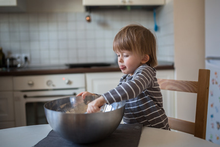 Toddler boy with a bowl in the kitchen making dough, childhood, real interior, toning, lifestyle, soft focusの写真素材