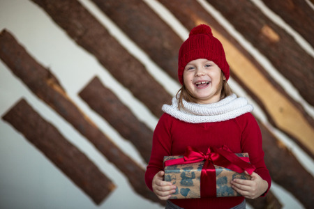 funny girl child  in red hat with present, lifestyle, real interior, winter rustic style,  brown...