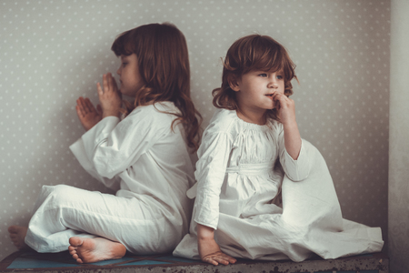 siblings sisters in nightgowns quarrel, swear and play on an old trunkの写真素材