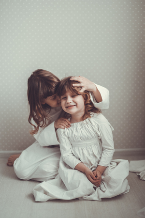 gentle sister girls in nightgowns retro, talking and hugging on chestの写真素材