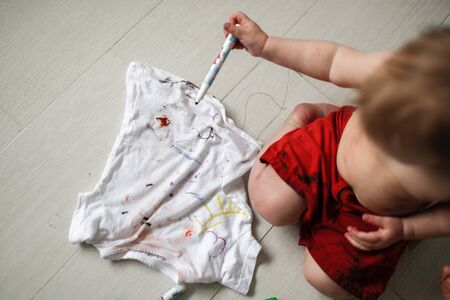 grimy  child paints marker on  T-shirt  in red trousers on a light background,の写真素材
