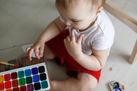 smutty kid Toddler paints watercolors eggs in red trousers on a light background,の写真素材
