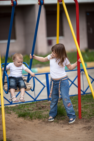 Older sister on  swing little sister, street, playground, helpの写真素材