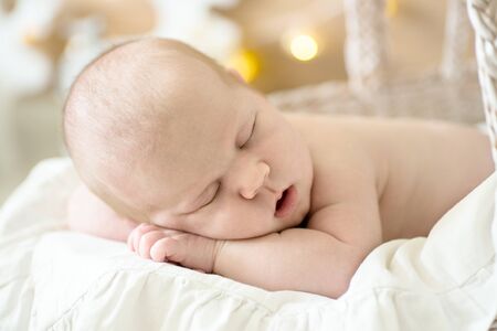 Charming baby, sleeping on his stomach in a wicker stroller, light cream real background, close-upの写真素材