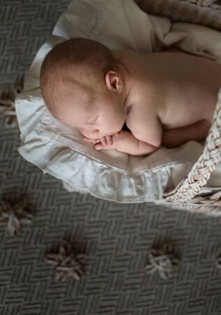 Charming baby, sleeping on his stomach in a wicker stroller, light cream real background, close-up