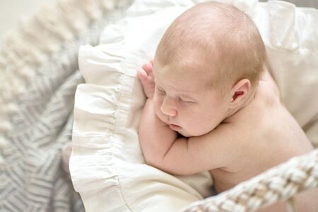 Charming baby, sleeping on his stomach in a wicker stroller, light cream real background, close-up