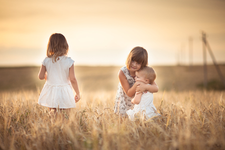 Three girls sisters walk in the field with rye at sunset, happiness and freedom, lifestyle and selective focusの写真素材