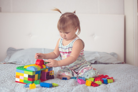 Toddler baby girl with funny tails playing with a constructor, lifestyle in a real interior, light background, toningの写真素材