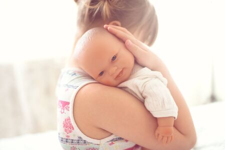 Girl kid cares about a doll, close-up, lifestyle in a real interior, light background, toning, selective focusの写真素材