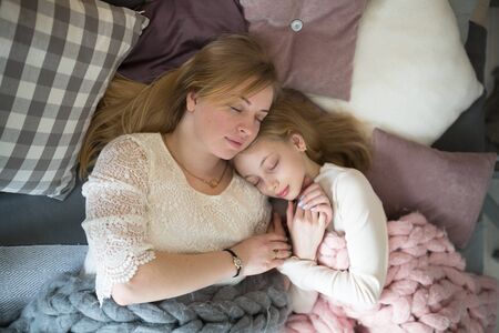 Beautiful young mom and her daughter teenager with long blond hair sleeping embracing, lifestyle, real interiorの写真素材