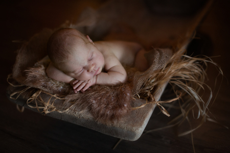 Charming newborn baby lying on stomach in a wooden box, brown background, straw, close-up and copy spaceの写真素材