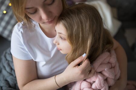 A beautiful mother hugs and gently strokes the daughter of a teenager, mom and daughter with long blond hair, the concept of tenderness and mutual understandingの写真素材
