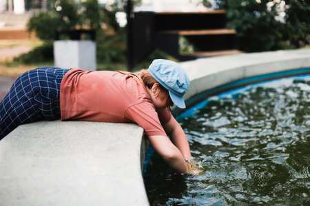 Happy European children play with water in the city fountain, child safety and freedom in the city. Summer walks with children around the town.の写真素材