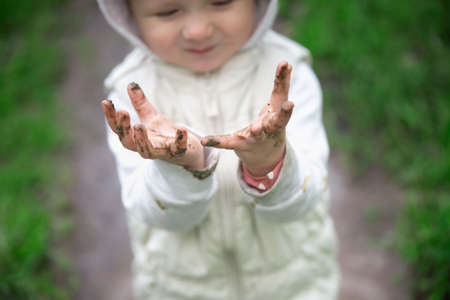 Cute child toddler in a warm vest and jacket stands in yellow rubber boots in a large puddle, Free children's walks in nature, mud and puddlesの写真素材