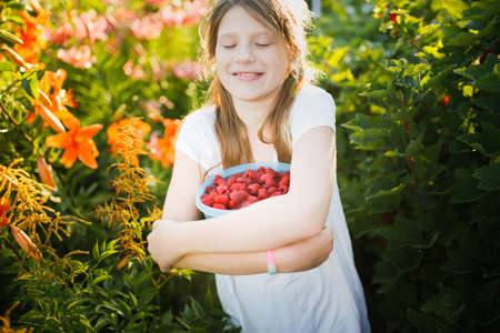 Cute European girl child teenager with big bowl of raspberries, Daughter helps pick berries in...