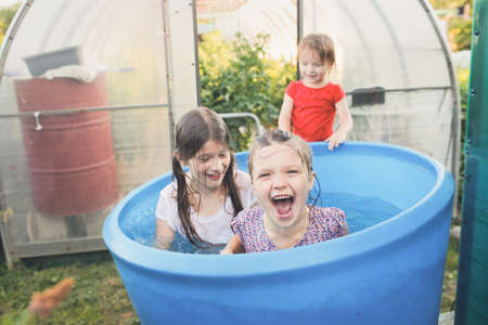 Wet happy children in the garden are bathing in a big blue barrel. Happy childhood in the countryside, swimming in the backyard in the heat.の写真素材