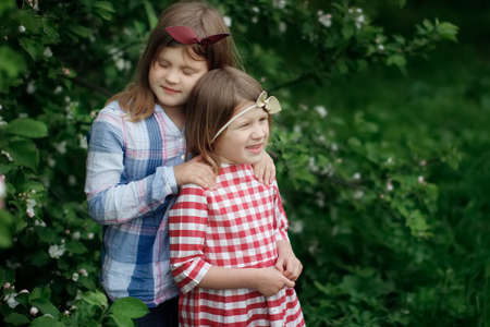 Cute sibling sister girls with a headband with a bow are hugging among greenの写真素材