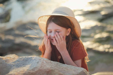 Cute european teenage girl in hat closes her eyes with her hands, summer vacation and childhoodの写真素材