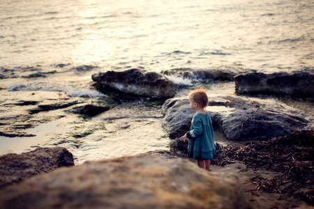 Child girl toddler in a casual dress made of muslin on the sea, a child walks along the beach near the sea, near the waterの写真素材