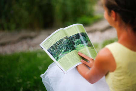 Cute european girl woman looking at gardening magazine in beautiful garden, landscaping art and well maintained gardenの写真素材