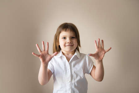 A child in a white T-shirt shows numbers on his fingers, beige backgroundの写真素材