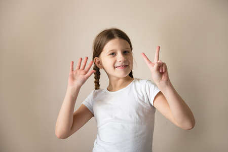 A child in a white T-shirt shows numbers on his fingers, beige backgroundの写真素材