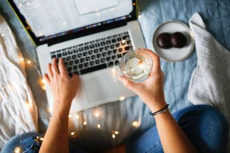 Woman working with laptop on bed with glass of champagne, top view. natural linen bedspreadの写真素材