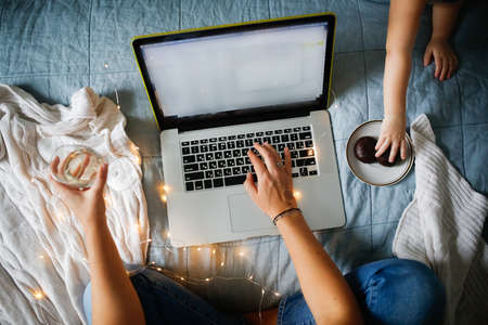 Woman working with laptop on bed with glass of champagne, top view. natural linen bedspread