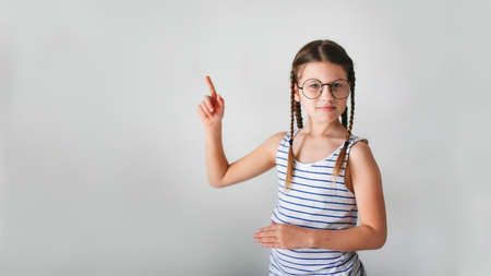 Girl child schoolgirl with pigtails in round glasses shows a finger, copy space and a light beige backgroundの写真素材
