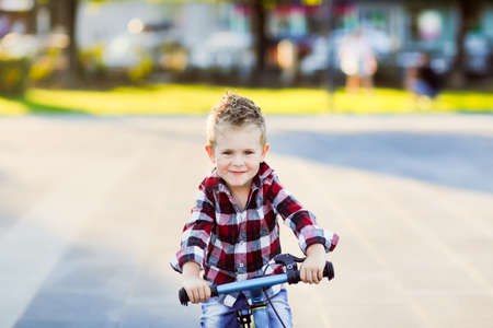 stylish European boy in shirt and jeans rides balance bike on asphalt. Child riding without helmetの写真素材