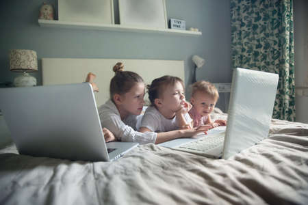 Children with laptops on bed in real bedroom at homeの写真素材