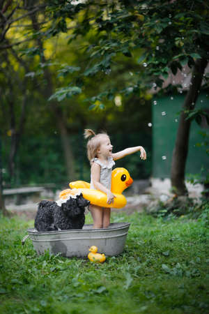 cute child with yellow inflatable duck bathes in iron tub with black pet poodle. Summer time and pets and children.の写真素材