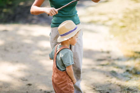 Mom and son in park among grass are playing fishing with stick and fishing rod. Mom hugs boy, helps...