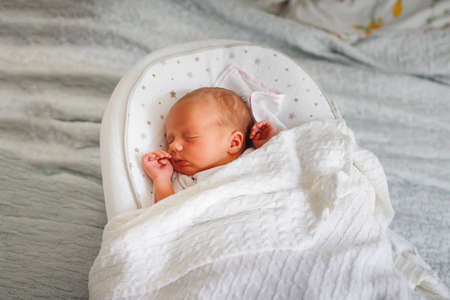 Newborn baby sleeps on cocoon on bed, wrapped in knitted blanket. cozy bright photo with newborn baby 5 daysの写真素材
