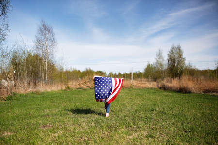 Happy American kid girl waving USA flag on independence day. Child running with the USA flag at a picnic on July 4thの写真素材