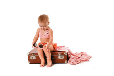 Amusing funny Little Toddler in a bathing suit and sunglasses with a retro suitcase, isolate on a white background. Travel concept with children, travel fees and dreams of the seaの写真素材