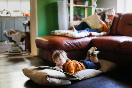 Funny children read books on soft mattresses on the couch and on the floor, real interior, dark styleの写真素材