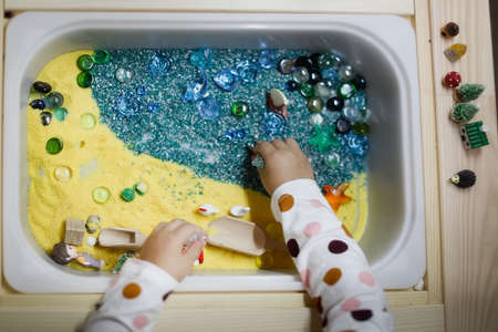 Sensory development box, sea theme with sand and stones, development of fine motor skills in children, close-up toys in touch tableの写真素材