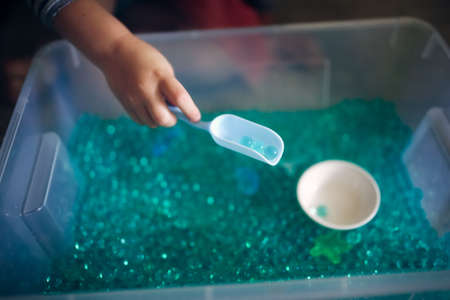 A child's hand reaches for a spoon in a plastic container.の写真素材