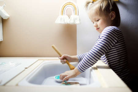 Cute little girl washing dishes in the kitchen at home.