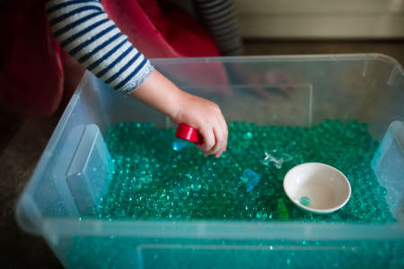 Little girl playing with colorful glass beads in a box.の写真素材