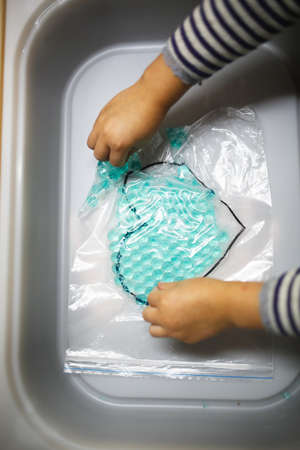 A child's hand puts a medical mask in the trash can.