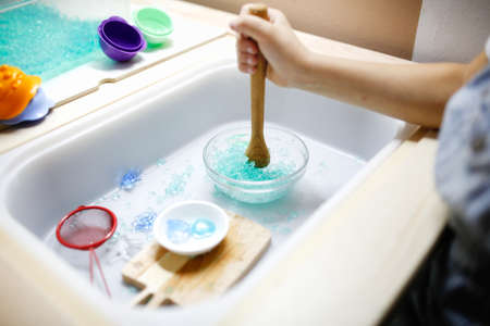 Close-up of a child's hands holding a wooden spoon and pouring water into a bowl.の写真素材