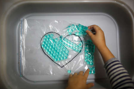 A child's hands hold a blue heart in a plastic bag.の写真素材