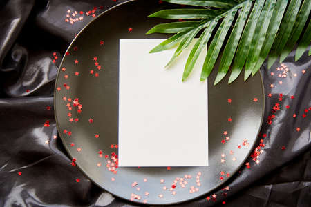 Elegant stationery card with tropical leaves on black plate. Festive creative mock up. Birthday card or advertising place with bright stars.の写真素材