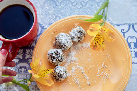 Healthy breakfast. Handmade candies in coconut shavings on orange plate and cup of coffee on ceramic...